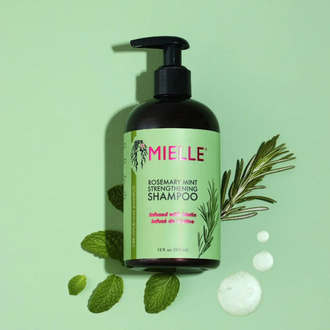 Mielle Rosemary Mint Strengthening Shampoo bottle with green leaves on a light green background