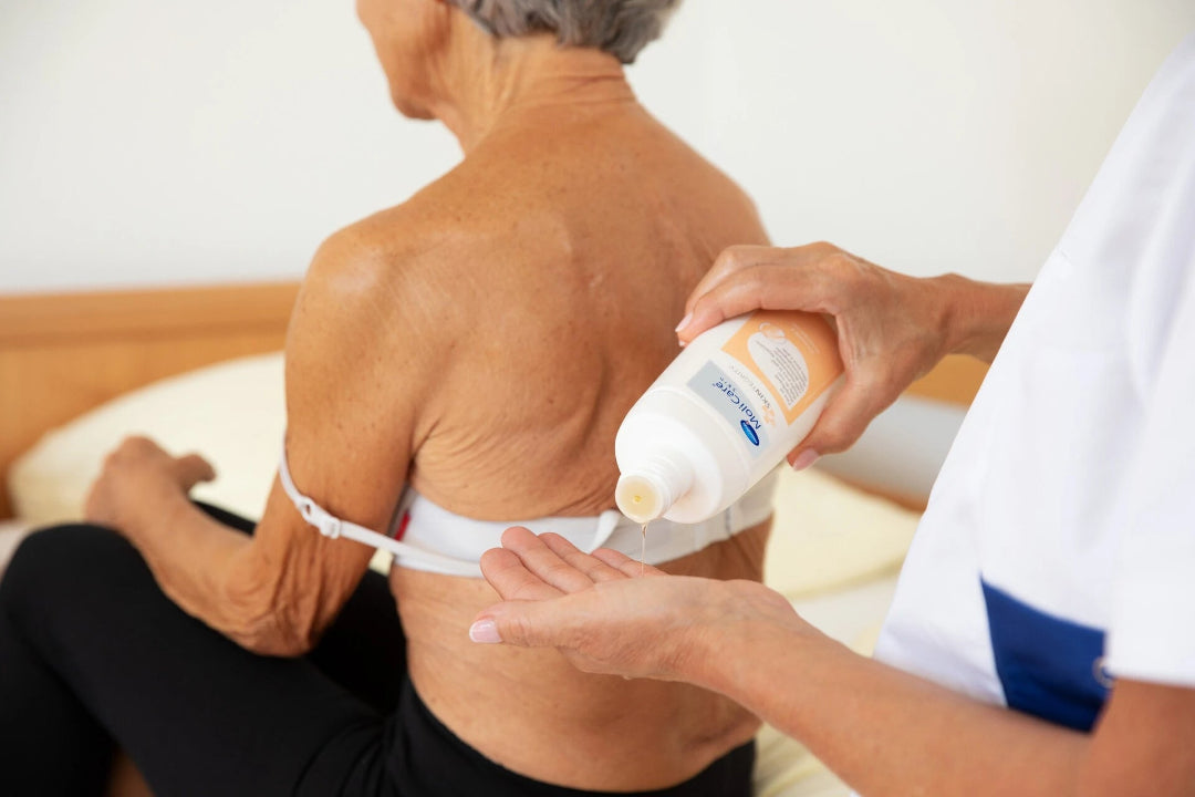 Person applying lotion to an elderly person's back