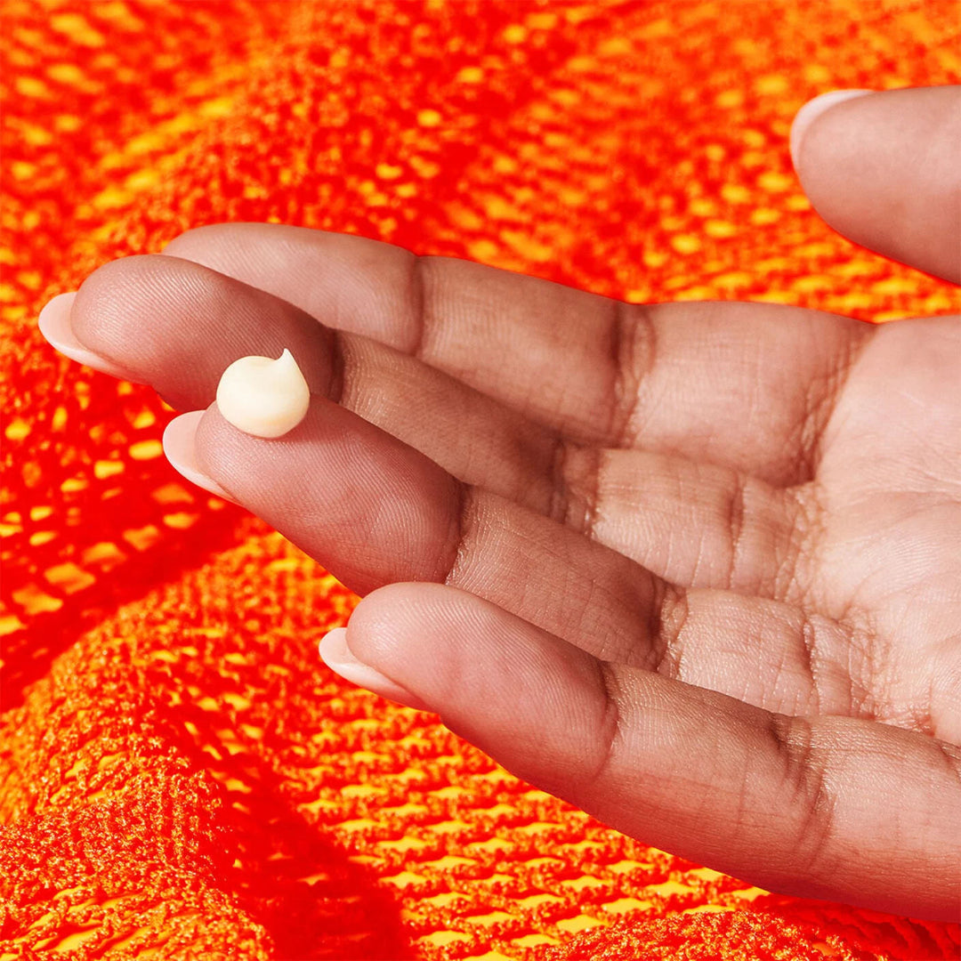 Hand holding a small white object against an orange textured background