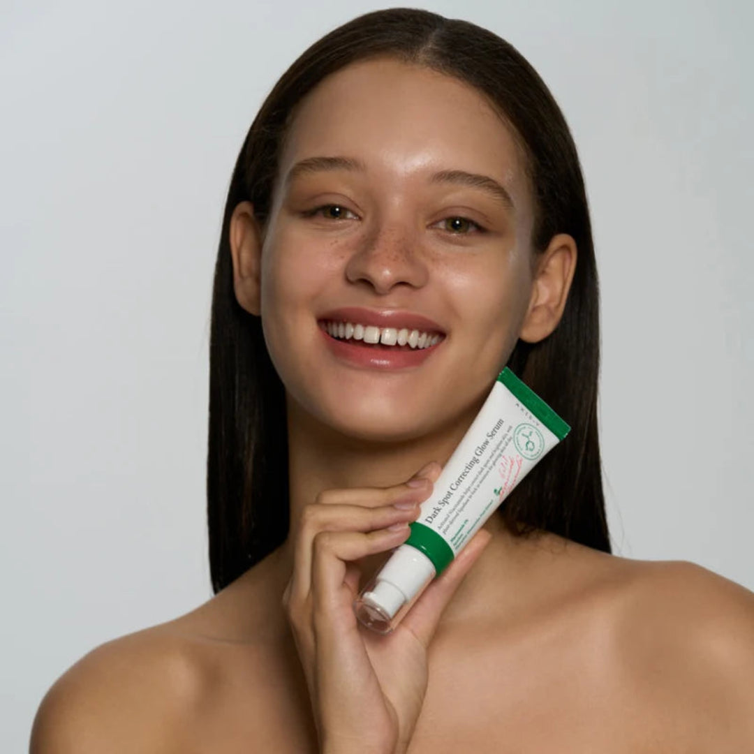 Woman holding a green and white tube of skincare product against a plain background