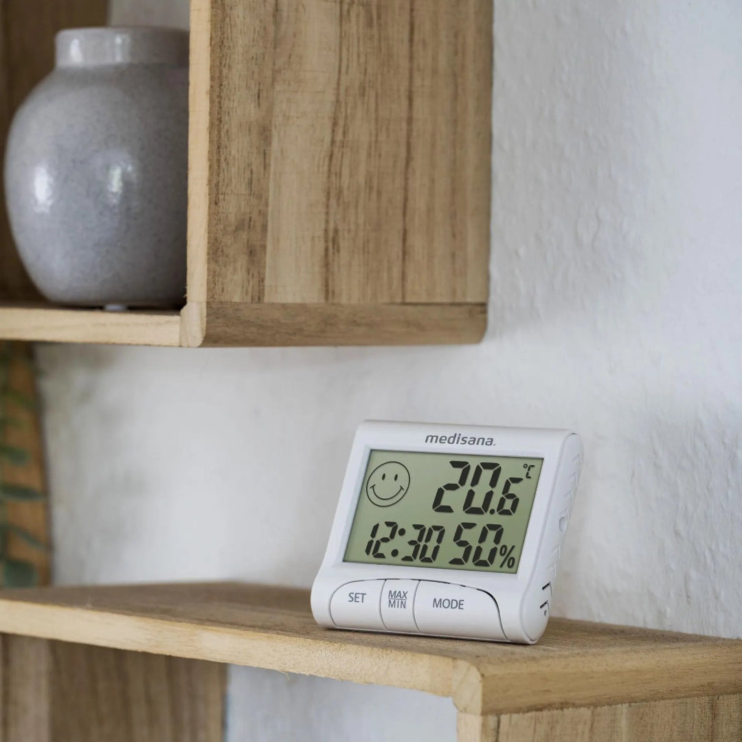 Digital thermometer with smiley face display on a wooden shelf