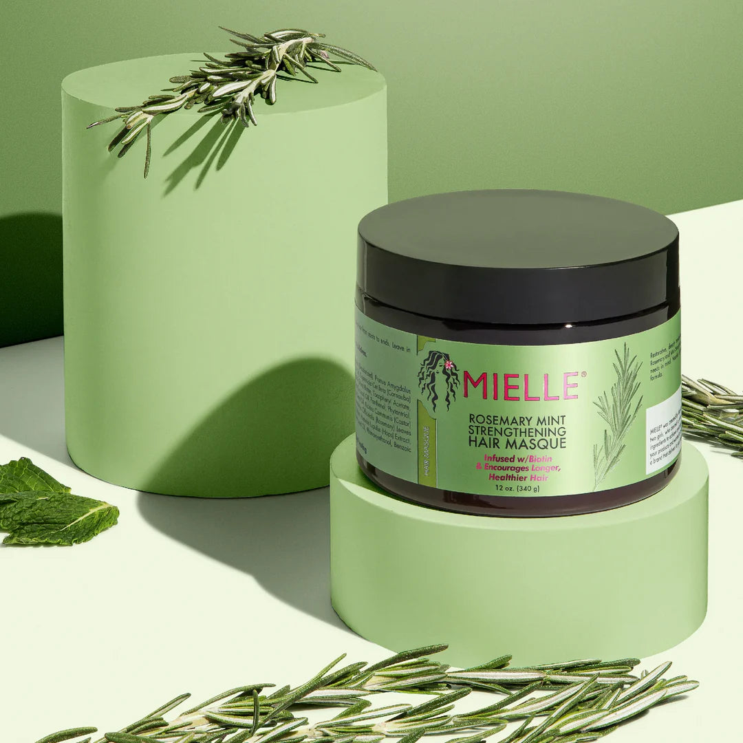 Mielle hair mask jar with rosemary and mint leaves on a green background