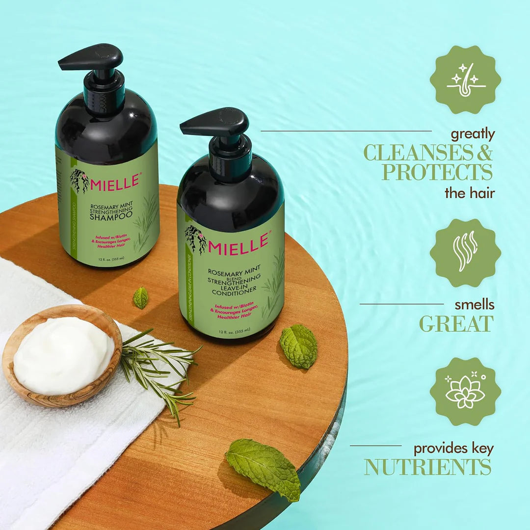 Two bottles of Mielle shampoo on a wooden board with green leaves and a towel, against a light blue background.