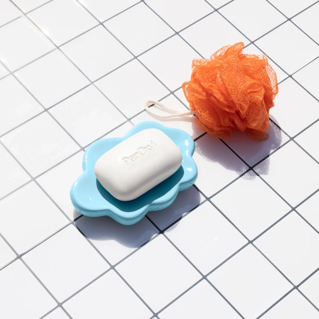 Bar of soap in a blue holder with an orange loofah on a tiled surface