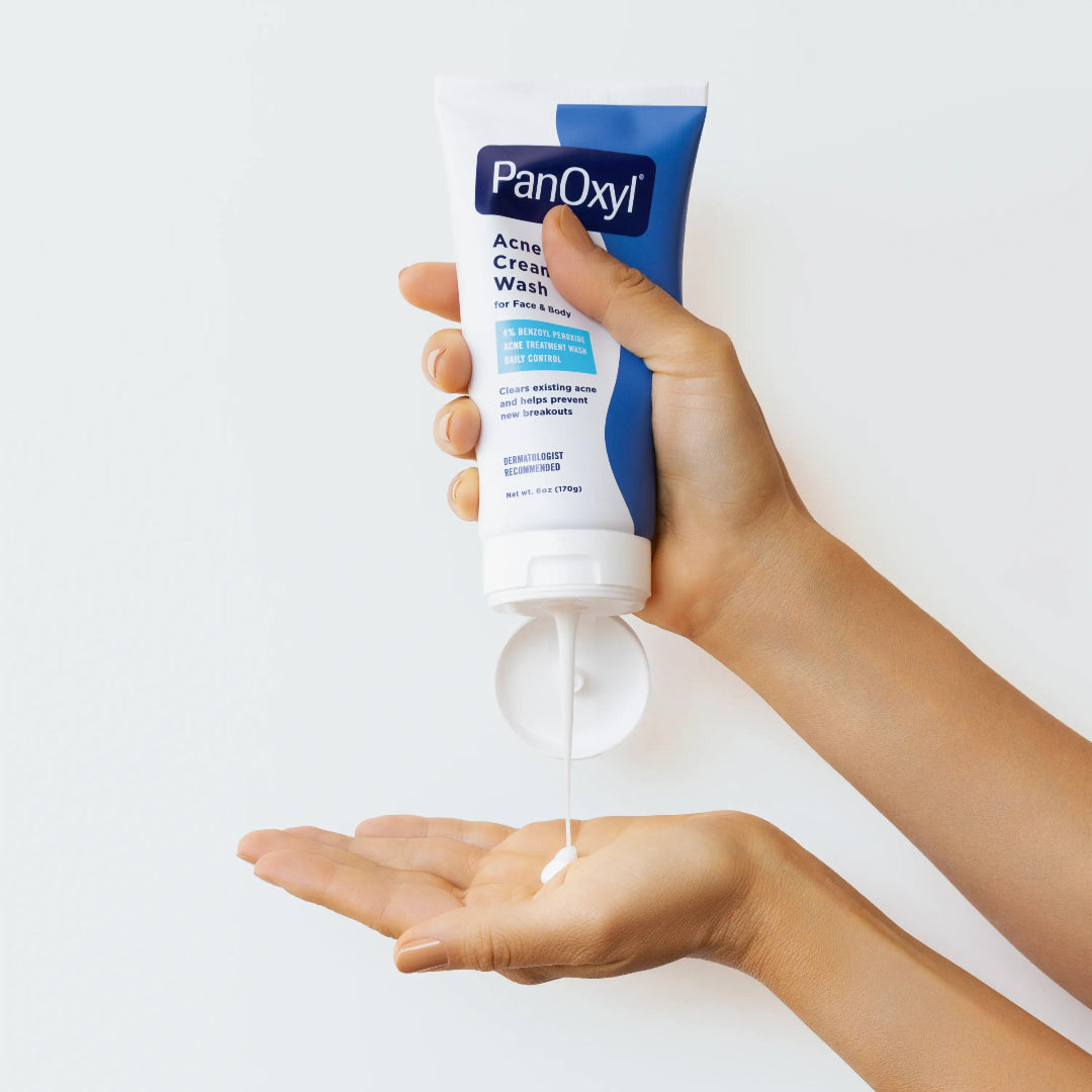 Hand holding a tube of PanOxyl Acne Cream Wash with a white background