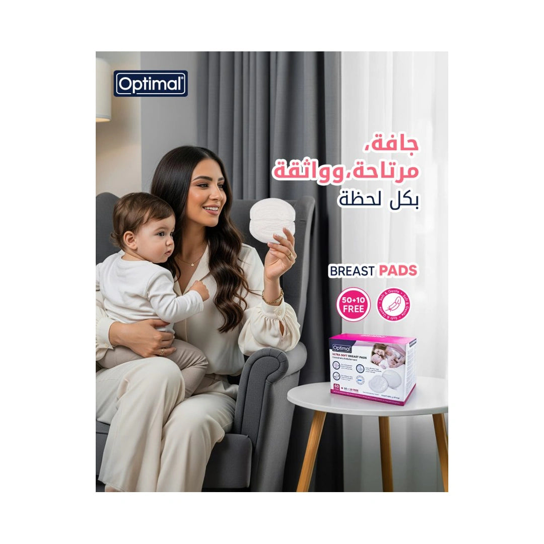 A woman in a gray armchair holding a baby while demonstrating a breast pad, with a product box labeled Optimal Breast Pads on a side table. The image includes Arabic promotional text and the Optimal brand logo.